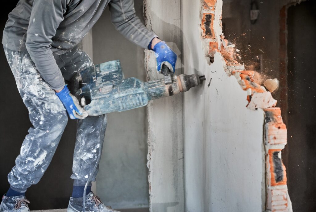 Male worker in work gloves drilling wall with hammer drill.