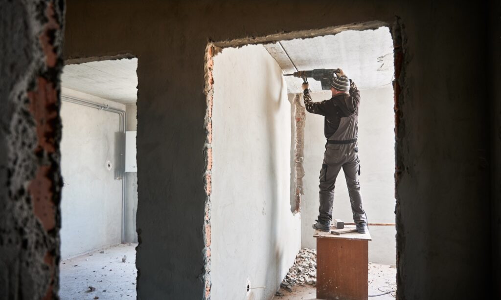 Overhaul of premise. Worker dismantling wall with jackhammer.